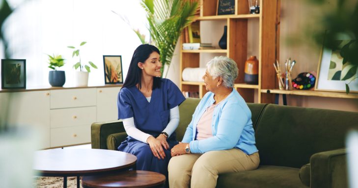 A healthcare professional talking with an elderly woman in a comfortable living space.